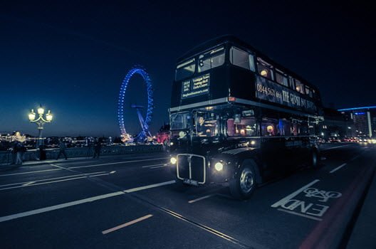London bus at night on London Bridge with the Big wheel lit up in blue in background