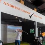 man in grey top swinging golf club in golf simulator