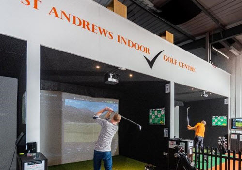 man in grey top swinging golf club in golf simulator