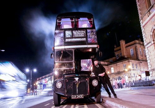 bus conductor leaning on front of a lit up bus at night with historic building lit up in background
