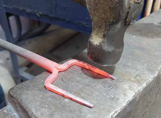 red iron fork tip on on bench with metal hammer head over it