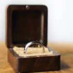 silver ring in a brown box with beige material setting and box sitting on wood background