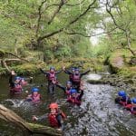 people in wet suits in river